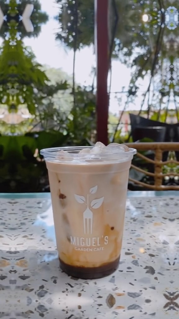 Iced coffee served in a branded Miguel's Garden Cafe cup with garden greenery visible in the background